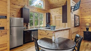 Een houten hut interieur met een keuken, eethoek en een groot raam dat voor natuurlijk licht zorgt.