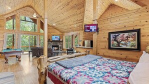 Een knus vakantiehuis met houten inrichting, een open haard, een pooltafel en een groot bed met een kleurrijke quilt.