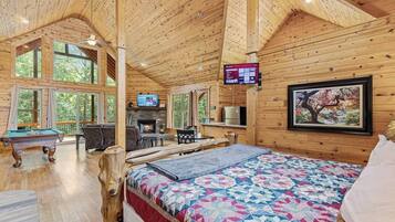 Una cabaña acogedora con interior de madera, chimenea, mesa de billar y una cama grande con colcha colorida.