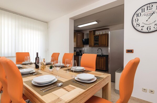 A dining area with a wooden table set for four, orange chairs, and a kitchen visible in the background.