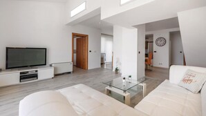 Ein modernes Wohnzimmer mit Fernseher, Glastisch und weißem Sofa.