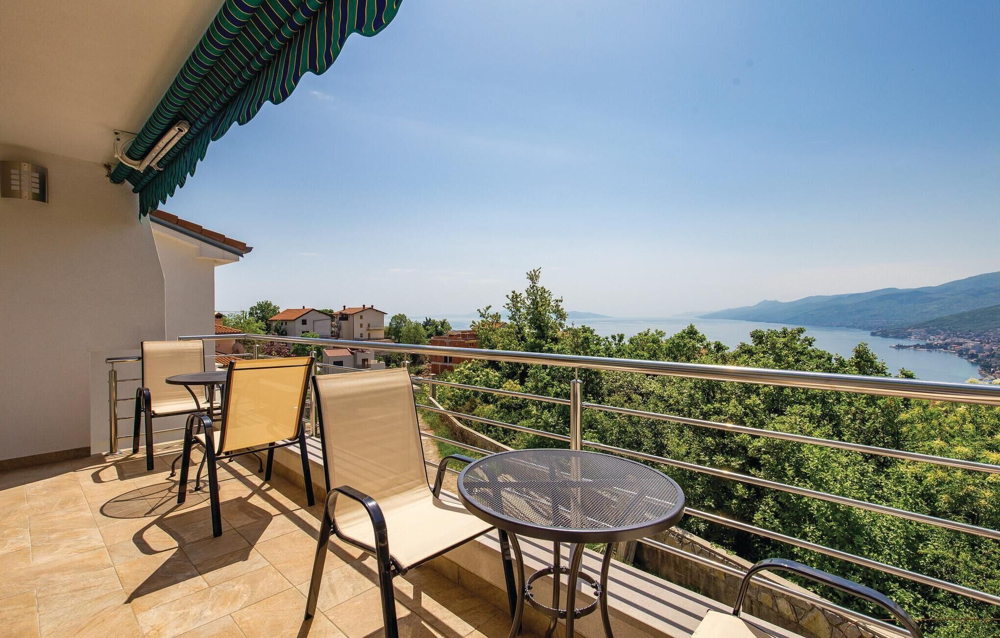 A balcony with a table and chairs, overlooking a lake and a town.
