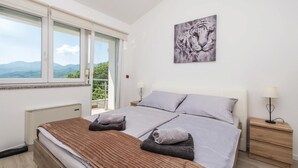 Ein Schlafzimmer mit einem Bett, zwei Kissen, einem Nachttisch mit Lampe, einem Heizkörper und einem Fenster mit Bergblick.