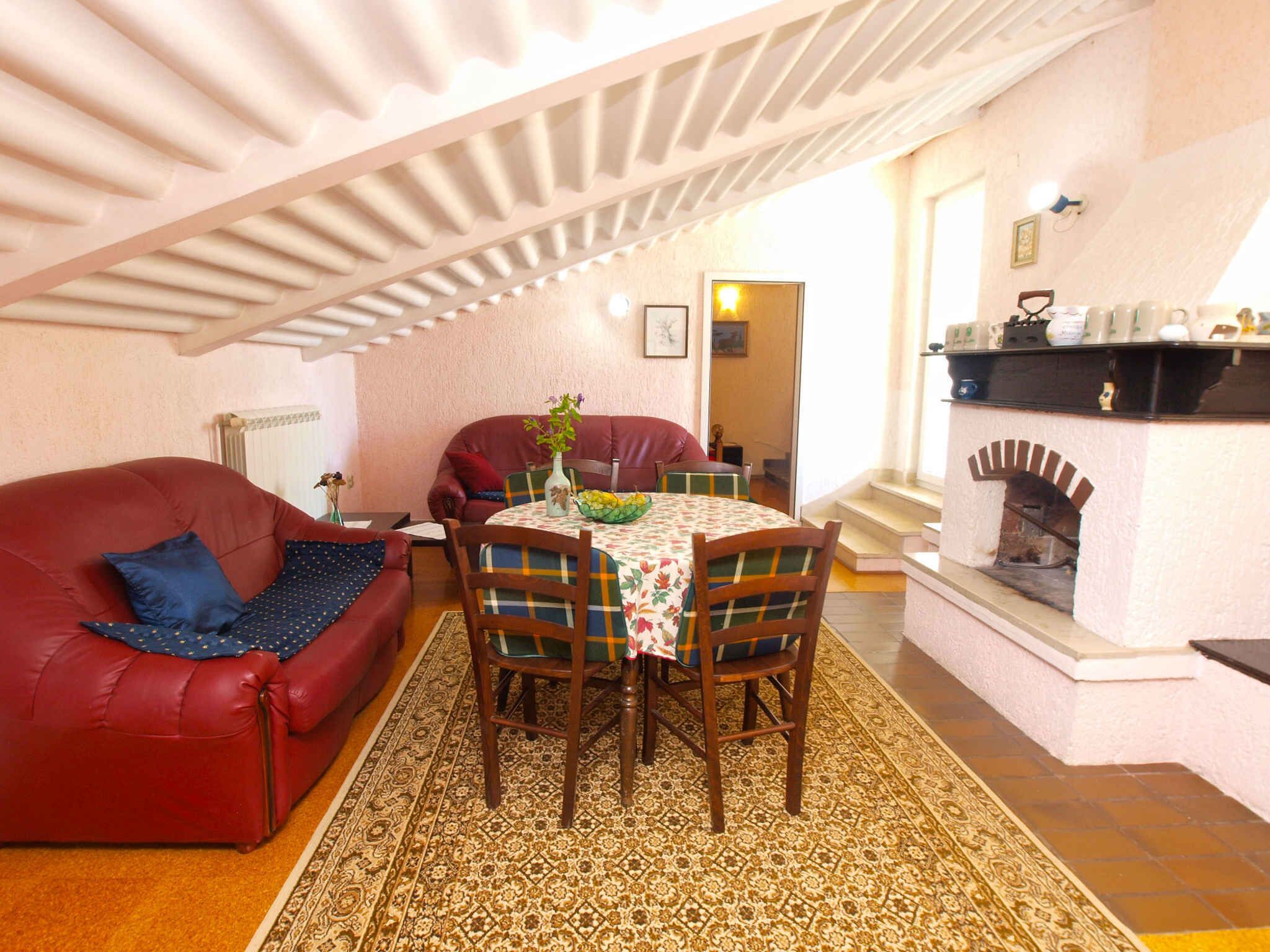 Una sala de estar acogedora con un sofá rojo, una mesa de comedor con sillas, una alfombra estampada y una chimenea.