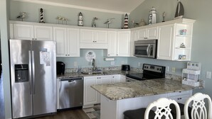 A modern kitchen with white cabinetry, stainless steel appliances, and decorative items on the shelves. - Beach Front Condo With Wonderful Ocean View  (Indian Beach)