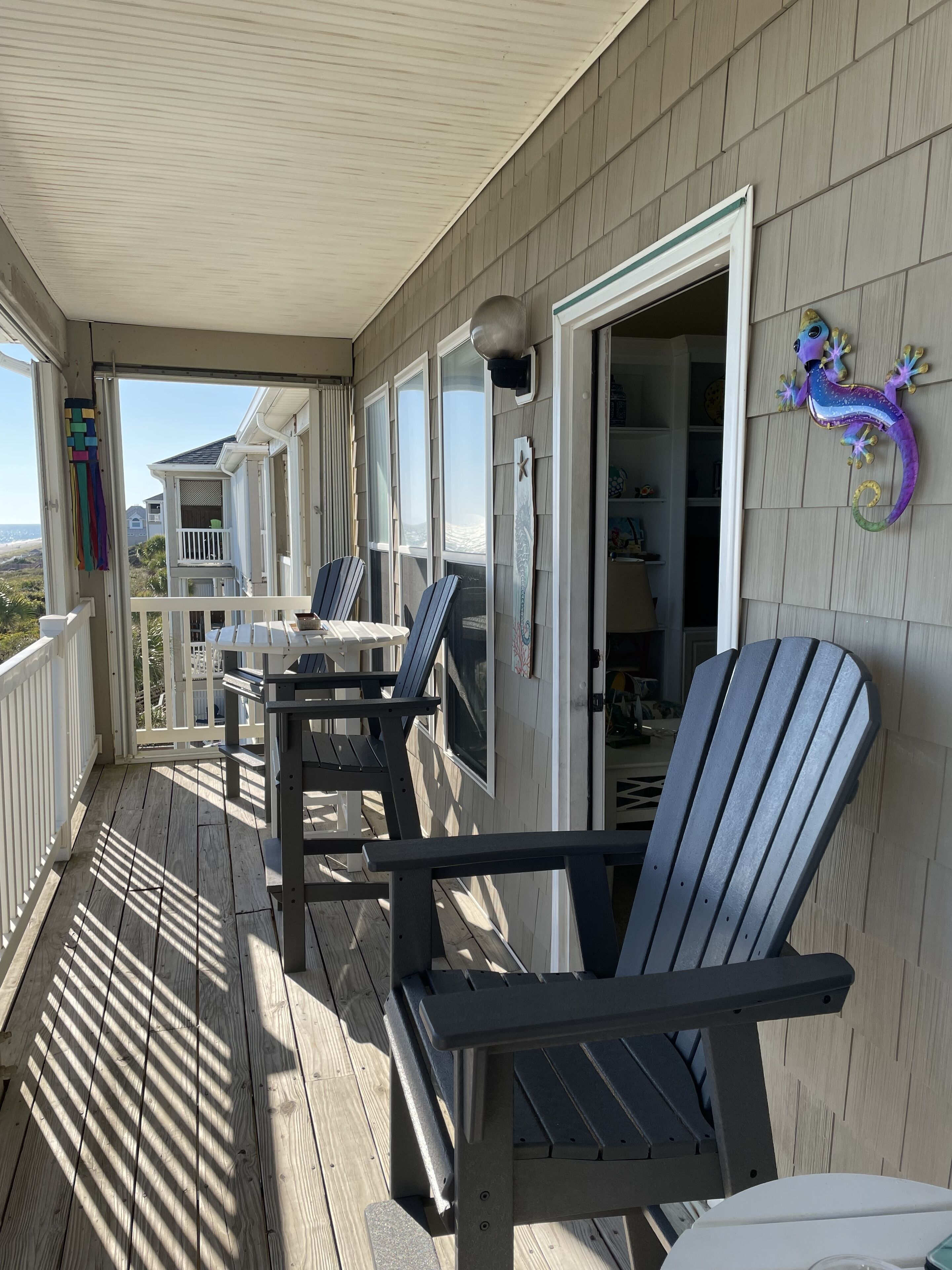 A covered porch with Adirondack chairs, a table, and a view of the beach.