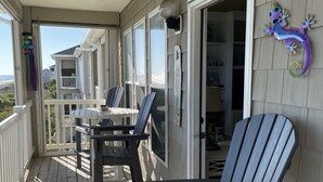 A covered porch with Adirondack chairs, a table, and a view of the beach. - Beach Front Condo With Wonderful Ocean View  (Indian Beach)