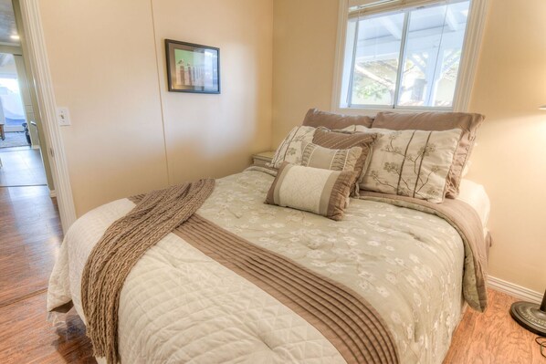 A bedroom with a bed, pillows, a blanket, a picture on the wall, and a window.
