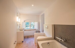 Une salle de bain avec une baignoire, un lavabo, une fenêtre et un espace douche.