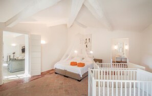 Une chambre à coucher comprenant un lit, un berceau, une salle de bain avec un lavabo et un miroir, et une porte donnant sur une autre pièce.
