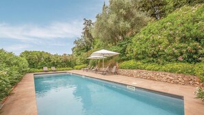 A rectangular swimming pool with a stone border, surrounded by lush greenery and a stone wall. - Awesome home in Lari -PI- (Lari -PI-)