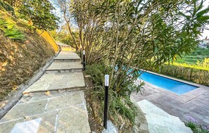 Stroll along the stone pathway to the inviting pool area surrounded by lush greenery.