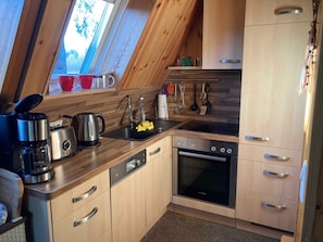 Eine Küche mit Holzausstattung, einem Bosch-Ofen, einer Kaffeemaschine und Küchenutensilien, die an der Wand hängen.