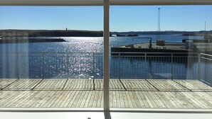 Une vue depuis un balcon doté d’une terrasse en bois, donnant sur une marina où sont amarrés des bateaux, avec un ciel bleu dégagé.