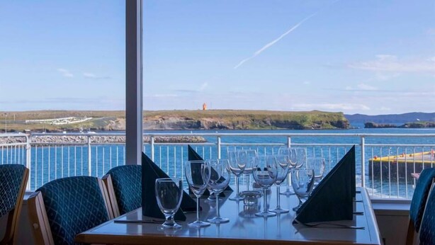 Une table à manger, ornée de plusieurs verres à vin et d’un menu, le tout mis en valeur par une vue panoramique sur la côte.
