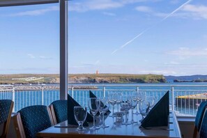 A dining table with multiple wine glasses and a menu, set against a scenic coastal view.