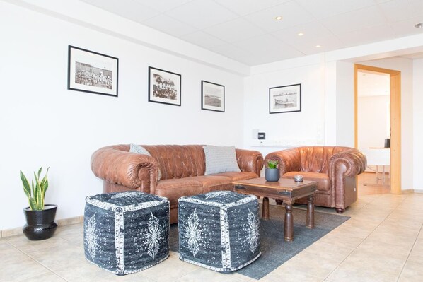A modern living room with a brown leather sofa, two decorative ottomans, a coffee table, and framed pictures on the wall.