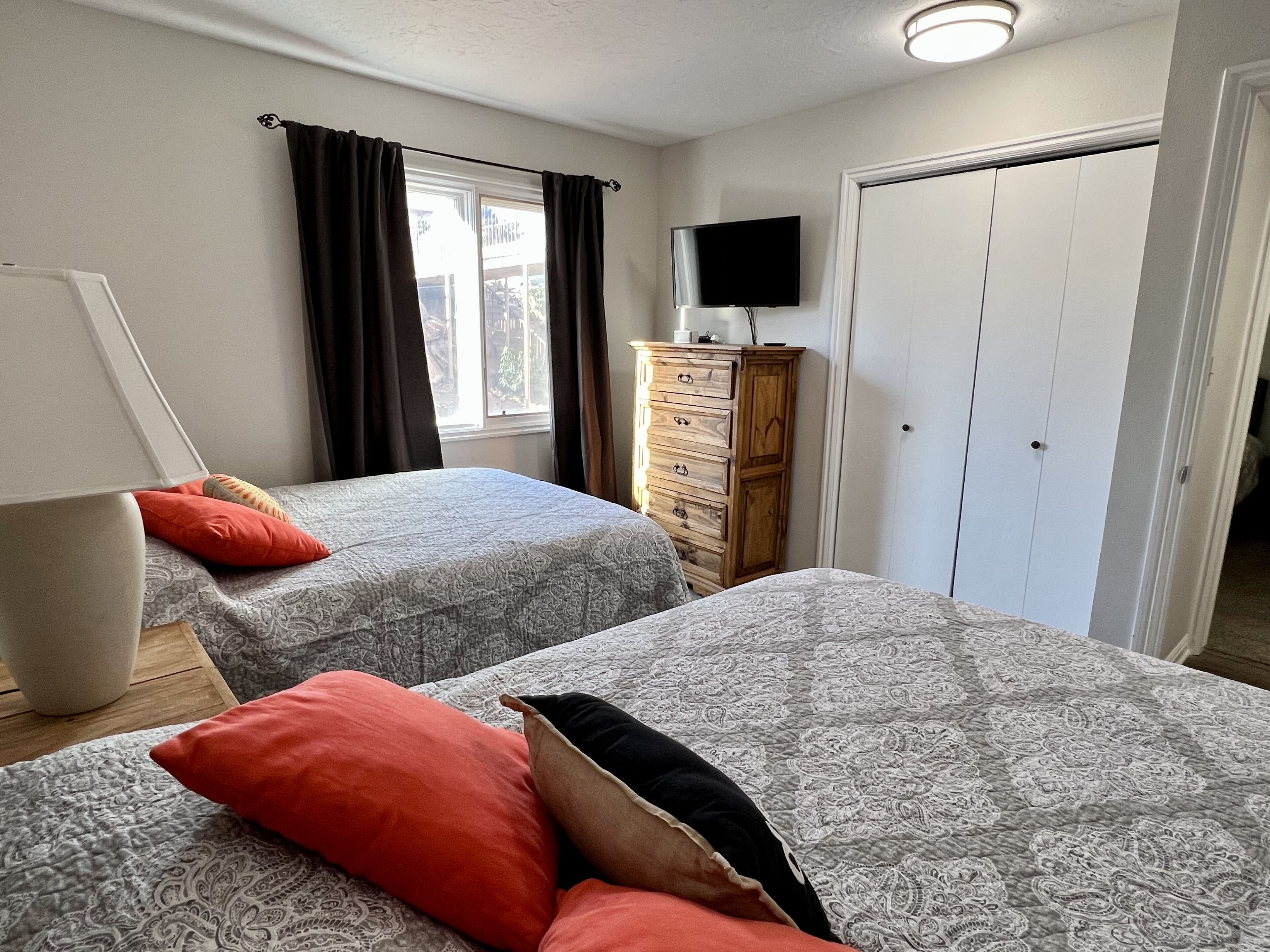 A bedroom with two beds, a dresser, a TV, and a window with curtains.
