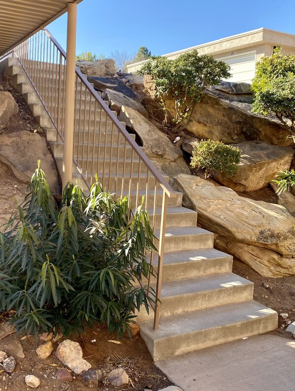 Una escalera de hormigón con barandillas de metal, rodeada de rocas y pequeñas plantas.