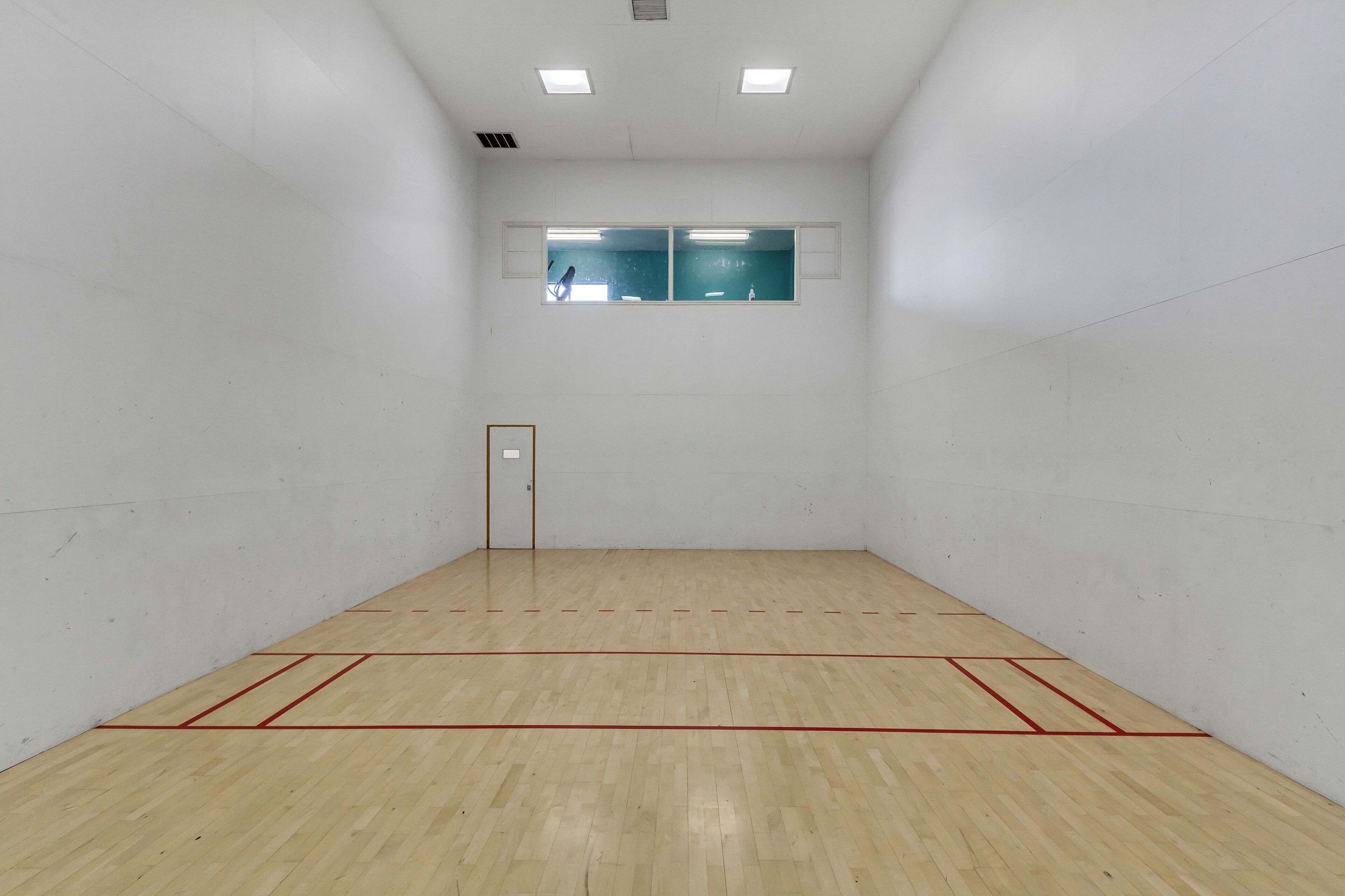 A squash court with a wooden floor, white walls, and a door.