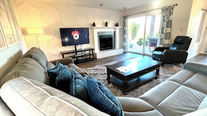 A modern living room with a sofa, a coffee table, a flat-screen TV, a fireplace, and a large window with curtains. - Sports Village Cliffside Getaway/3 bed/2 bath w/View located in St George, UT (St George)