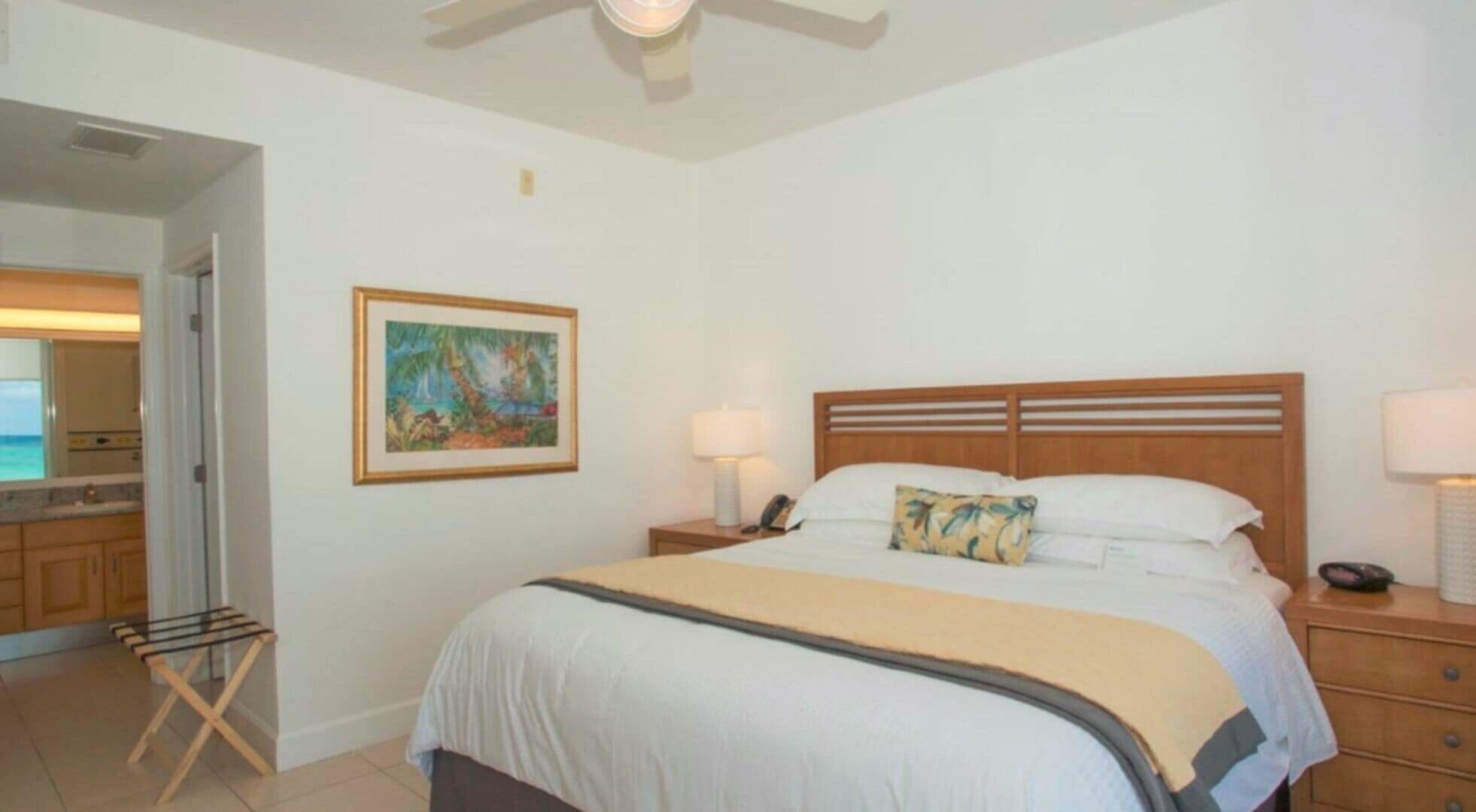 A hotel room with a bed, a nightstand, a lamp, a painting, and a drying rack.
