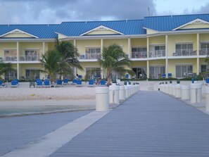 A hotel with a beachside location, featuring a boardwalk leading to the beach, multiple balconies, and outdoor seating areas.