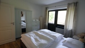 Quarto com cama, guarda-roupa, radiador e janela com cortinas.