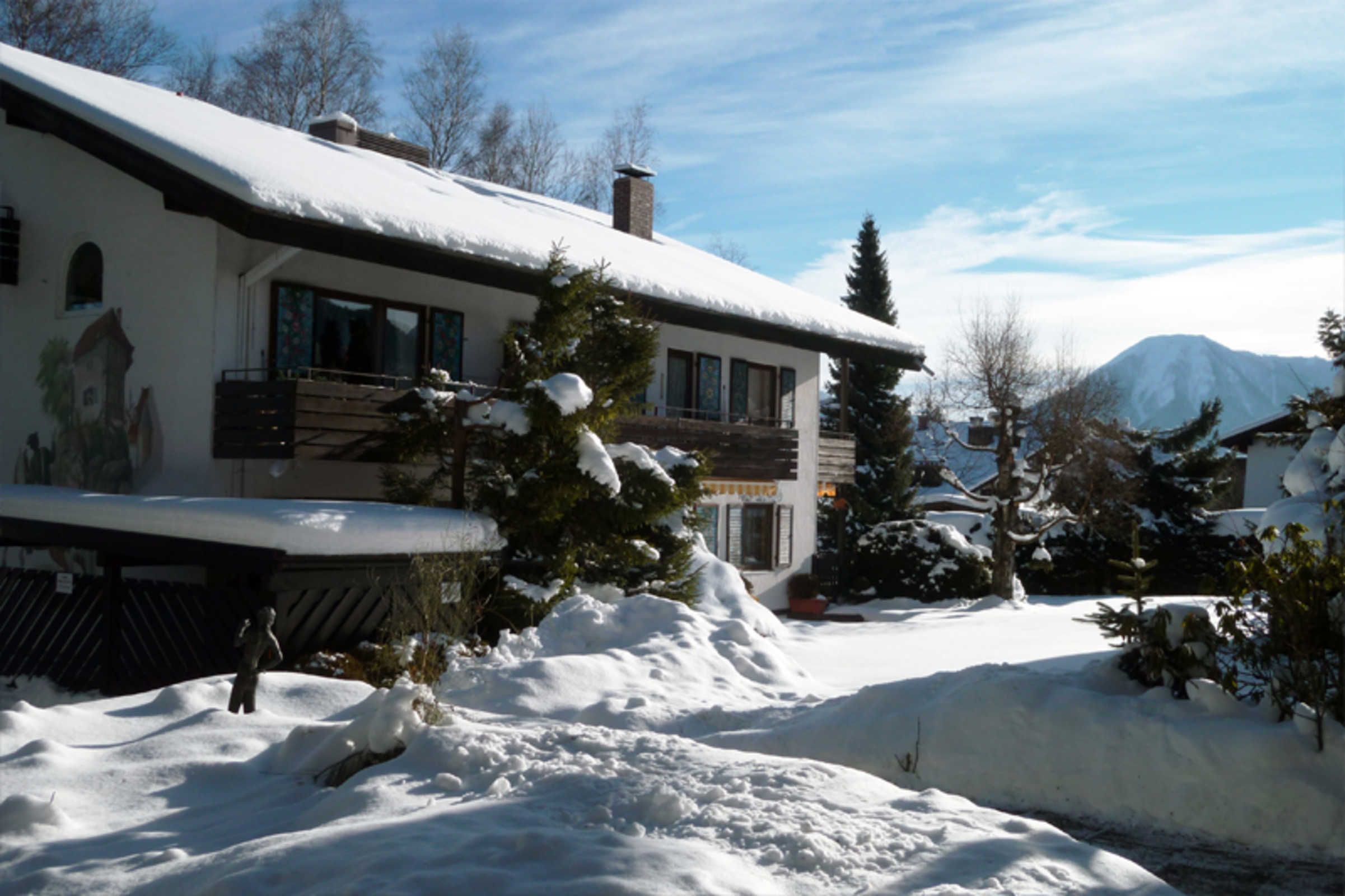 Ein mit Schnee bedecktes Gebäude mit einem Balkon, ein Berg im Hintergrund und schneebedeckte Bäume.