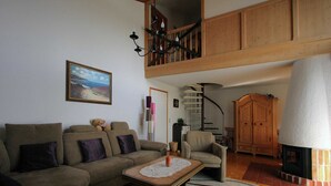 Uma sala de estar com sofá, mesa de centro, lareira, escada de madeira e um quadro na parede.