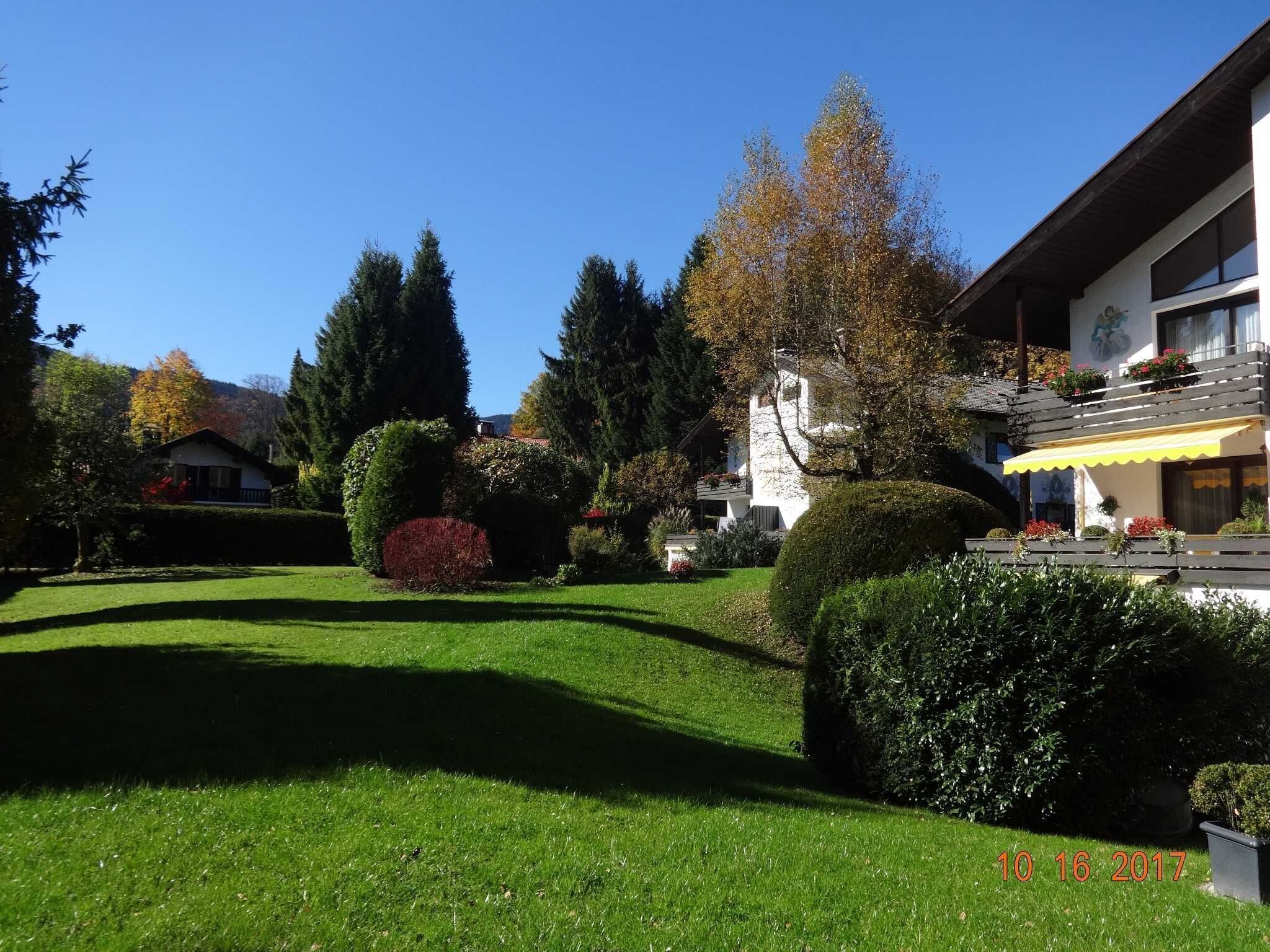 A well-maintained garden with neatly trimmed hedges, a variety of trees, and a clear blue sky.
