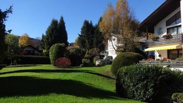 A well-maintained garden with neatly trimmed hedges, a variety of trees, and a clear blue sky.