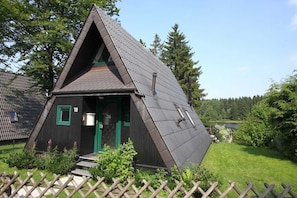 Ein dreieckiges Holzgebäude mit geneigtem Dach, einer grünen Tür und einer kleinen Veranda.