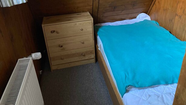 Ein kleines Zimmer mit einem Einzelbett, Holzwänden, einem Holzschrank und einem weißen Heizkörper.