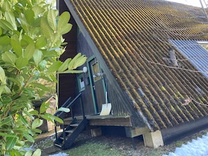Un edifici amb un teulat inclinat, una escala de fusta que condueix a una porta i una petita zona de porxo.