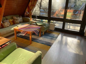 Ein gemütliches Zimmer mit einem grünen Sofa, einem Holztisch und Blick durch große Fenster.
