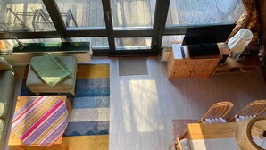 Ein gemütliches Zimmer mit einem großen Fenster, einem Streifenmuster-Teppich, einem kleinen Tisch, zwei Stühlen und einer Holzkommode.