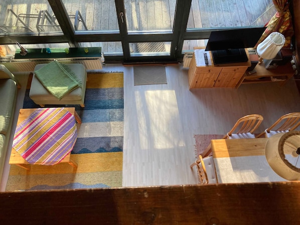 Ein gemütliches Zimmer mit einem großen Fenster, einem Streifenmuster-Teppich, einem kleinen Tisch, zwei Stühlen und einer Holzkommode.