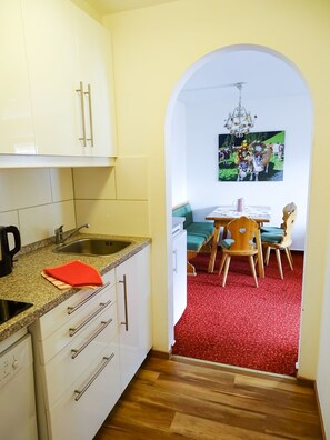 A kitchen with white cabinets, a granite countertop, and a red rug leading to a dining area with a table and chairs. - Apartment for 6 persons - Apartment house Kaltenbach-Stumm (Stumm)