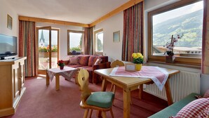 A cozy room with a dining table, a sofa, a TV, and large windows with a mountain view.