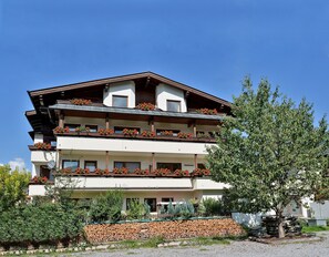A multi-story building with balconies, a stone wall, and a tree in the foreground. - Apartment for 6 persons - Apartment house Kaltenbach-Stumm (Stumm)
