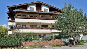 A multi-story building with balconies, a stone wall, and a tree in the foreground.