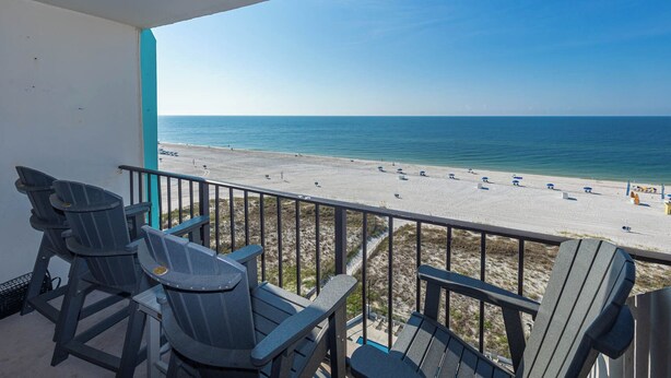 A balcony with three Adirondack chairs overlooking a beach.