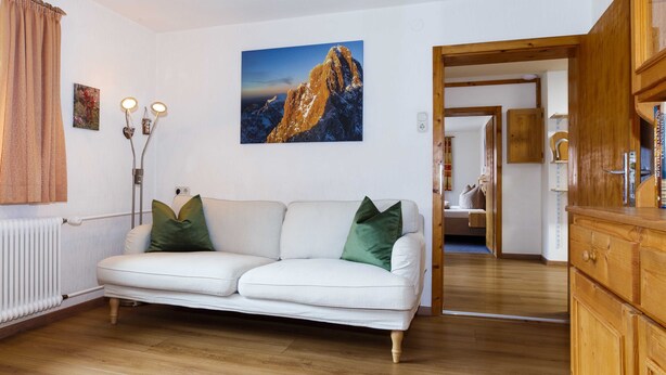 Ein Wohnzimmer mit einem weißen Sofa, einem Berggemälde und einem Holzkabinett.