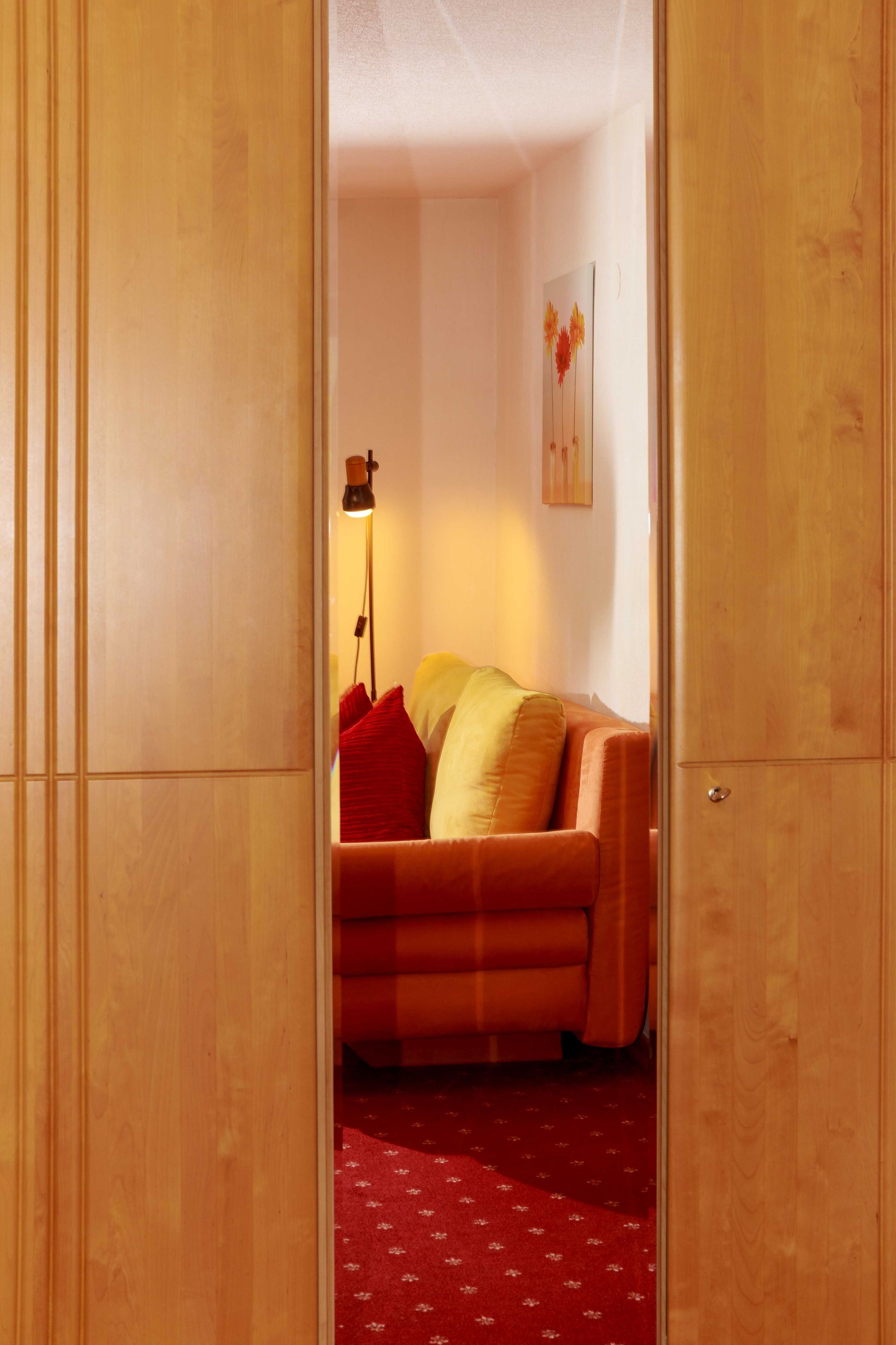 Una habitación con un armario de madera, un sofá con cojines, una lámpara de pie y una alfombra estampada.
