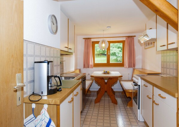 Cocina compacta con cafetera, lavabo y mesa de comedor con un bol de fruta.