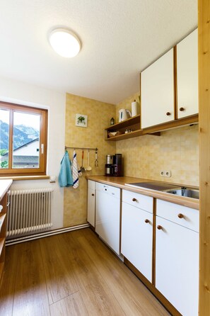 Cozinha com armários de madeira, janela, radiador e vista para montanhas.