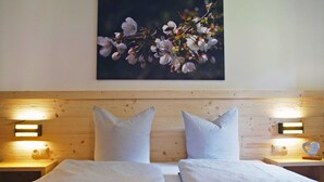 Ein Doppelbett mit zwei Kissen, ein Holzkopfstück, Nachttischlampen und ein an der Wand hängendes Bild mit Blumen.