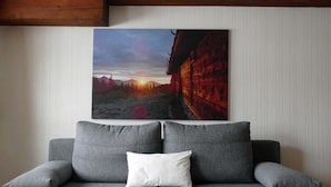 Ein graues Sofa mit einem weißen Kissen und einem Bilderrahmen mit einem Sonnenuntergang über einer Berglandschaft.