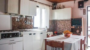 A kitchen with white cabinets, a stove, a table with a bowl of fruit, and a television on a stand. - Stunning home in Kornati with house sea view (Kornati)